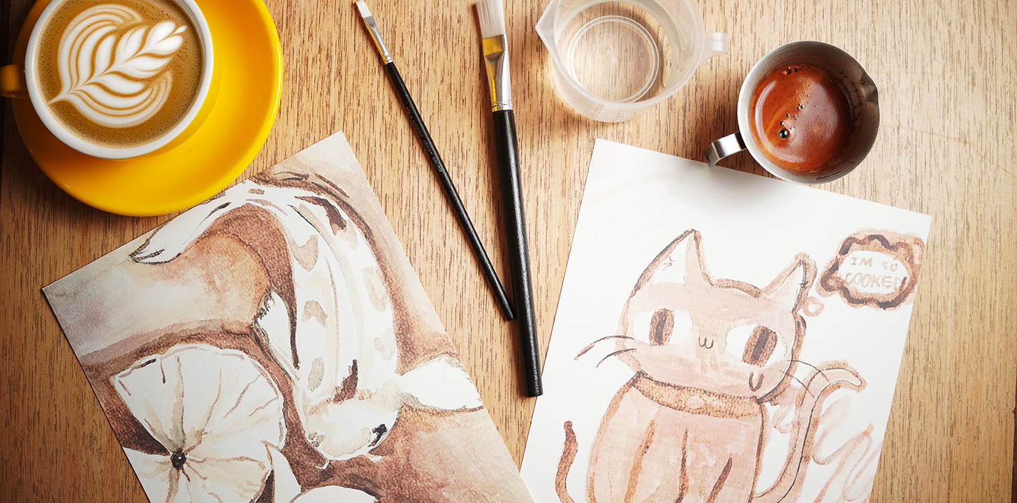 Workshop coffee paintings of a cat and flowers, with paintbrushes and coffee on a wooden table